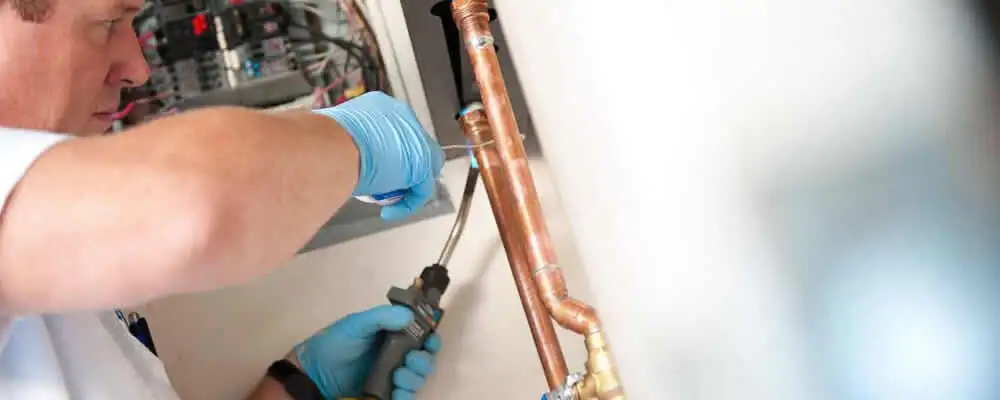 Water heater repair technician testing copper pipe connections and controls in Philadelphia, PA